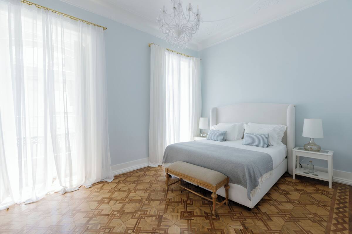 Un dormitorio con una cama grande, un banco, una mesita de noche y una araña.