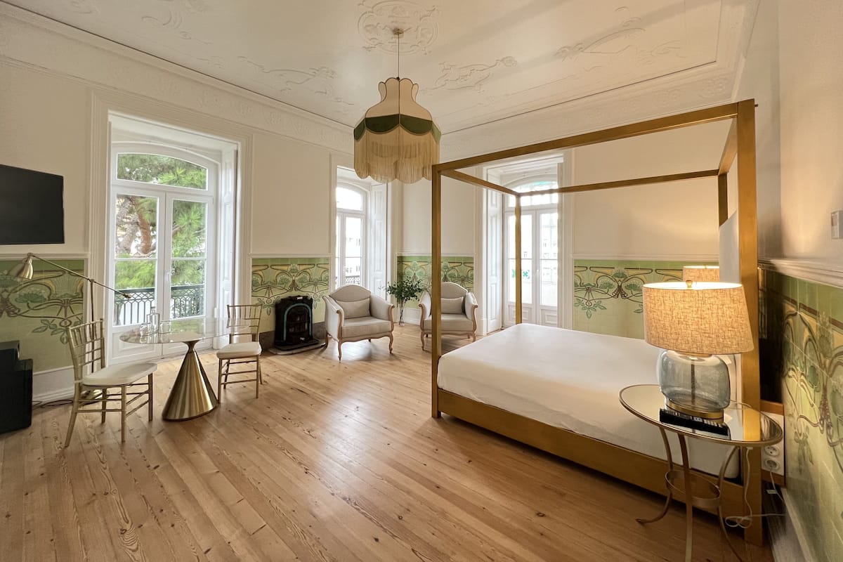 Un dormitorio amplio con cama con dosel, una zona de estar con sillas, televisión y ventanas grandes que ofrecen vistas al exterior.