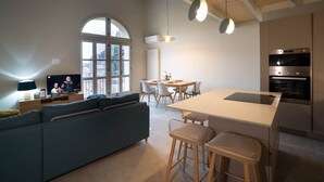 A modern kitchen with a central island, a dining area with a table and chairs, a blue sofa, and a TV in the living area. - Bright and exclusive apartment in the heart of Città Alta renovated to new (Bergamo)