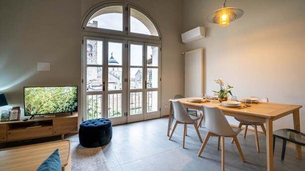 A modern living room with a TV, sofa, and ottoman. A dining area with a table and chairs is visible. - Bright and exclusive apartment in the heart of Città Alta renovated to new (Bergamo)