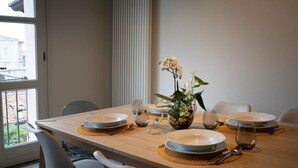 A dining table set for four with white plates, a vase of flowers, and a view of a building through a window. - Bright and exclusive apartment in the heart of Città Alta renovated to new (Bergamo)