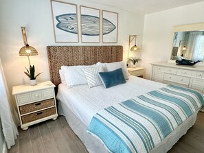 A neatly arranged bedroom with a large bed, a bedside table with a lamp, a mirror, and a wall-mounted artwork. - Beautifully Updated Naples Condo, Walk to Beach & 3rd St (Naples)