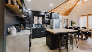 A modern kitchen with dark cabinetry, a wooden island, and a dining area with chairs.