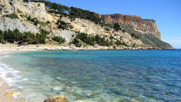 Une plage côtière aux eaux limpides, bordée de falaises rocheuses et dotée d’une végétation clairsemée.