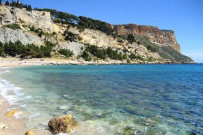 Una playa costera con aguas cristalinas, acantilados rocosos y vegetación escasa.