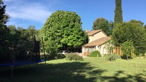 Une maison avec un grand arbre dans le jardin, un ciel dégagé et un grand arbre à droite.