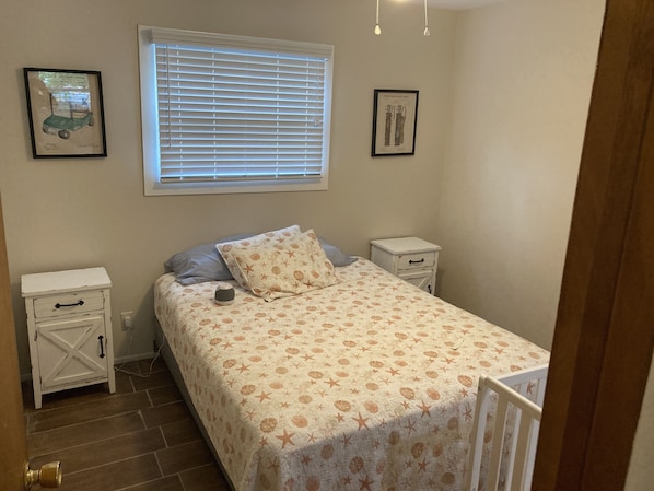 A bedroom with a bed, two bedside tables, a window with blinds, and two framed pictures on the wall.
