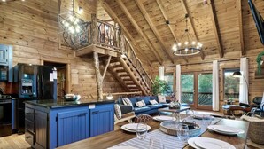 A spacious kitchen with a central island, a dining area with a wooden table, and a living room with a blue sofa. - Discounts 3+N 4BR Cabin Sleeps 10 Hot Tub, Game Room, Fire Pit, Fenced Yard-Pets (Blue Ridge)