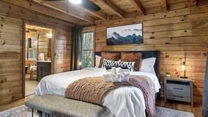 A wooden cabin bedroom with a bed, bench, bedside table, and a painting on the wall. - Discounts 3+N 4BR Cabin Sleeps 10 Hot Tub, Game Room, Fire Pit, Fenced Yard-Pets (Blue Ridge)