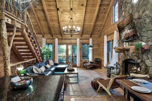 L’intérieur de cette vaste cabane en rondins comprend un grand salon, une cheminée en pierre, un coin repas et un escalier menant à un étage supérieur.