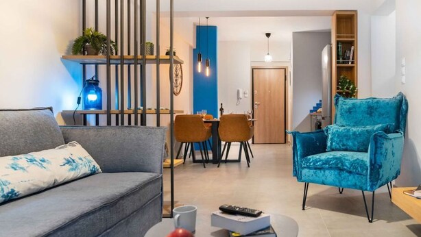 A modern living room with a grey sofa, a blue armchair, and a dining area with a table and chairs. - Suite 06 - Smart Cozy Suites - Cozy, elegant and near the metro (Kallithea, Athens)