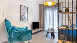 A modern living room with a teal sofa, a flat-screen TV, a small round table with a bowl, and a hanging light fixture. - Suite 06 - Smart Cozy Suites - Cozy, elegant and near the metro (Kallithea, Athens)