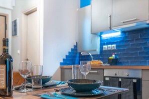 Una mesa de comedor dispuesta con platos, tazones y copas de vino, con una botella de vino y un frutero en la encimera.