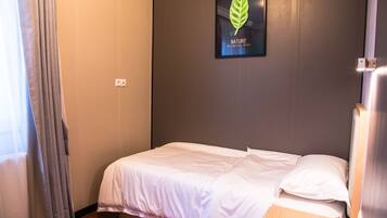 A single bed in a room with a grey wall and a framed botanical image.