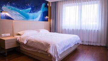 A hotel room with a large bed, a nightstand, a wall mural, and a window with sheer curtains.