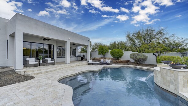 Una casa moderna con piscina, mobiliario exterior y un patio cubierto.
