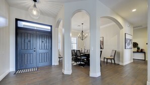 Un vestíbulo amplio con puerta de madera oscura, paredes blancas y una zona de comedor con candelabro.