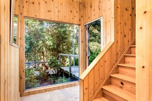 Stairs lead to a spacious upper level with a balcony offering views of the surrounding greenery.