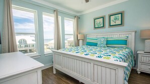 Ein Schlafzimmer mit einem Bett, zwei Fenstern, einem Deckenventilator und Bildern an der Wand.