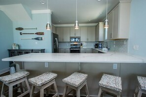 A modern kitchen with a large island, bar stools, and pendant lighting.
