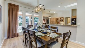 A dining area with a wooden table set for six, surrounded by chairs. There is a large window with curtains, a hanging light fixture, and a view of the outdoors. - Experience luxury at Sedona Chapel Area Charm, a spacious 4BR home with stunning red rock views. (Sedona)