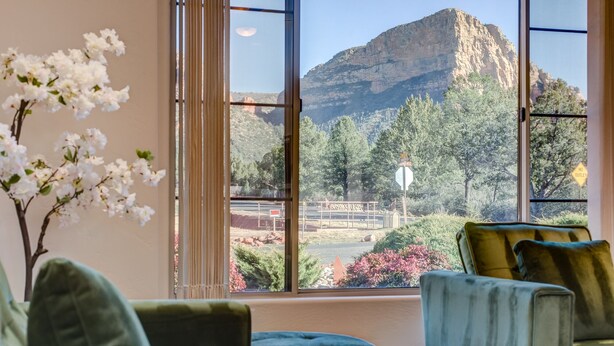 A room with a large window offering a view of a mountain and a road with a 'No Outlet' sign. There are two green upholstered chairs and a small ottoman. - Experience luxury at Sedona Chapel Area Charm, a spacious 4BR home with stunning red rock views. (Sedona)