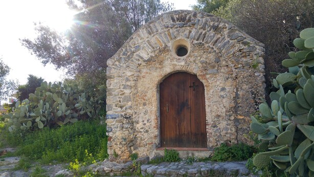 Une construction en pierre dotée d’une porte en bois, entourée de cactus et de verdure.