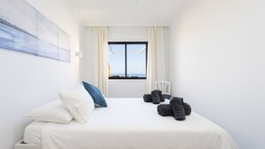 Ein Hotelzimmer mit Bett, einem Fenster mit Vorhängen, einem Sessel und einem Bild an der Wand.