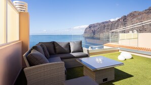Ein Balkon mit einer Sitzecke, einem Tisch und zwei weißen, kugelförmigen Objekten mit Blick auf eine Küstenlandschaft.