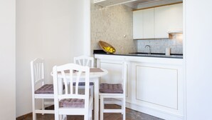 Eine moderne Küche mit weißen Schränken, einer Marmor-Spritzschutzwand und einer kleinen Essecke mit zwei weißen Stühlen und einem runden Tisch.