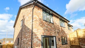 A two-story brick house with a large glass door and windows, a wooden fence, and a clear sky. - Larch Lodge (Totland Bay)