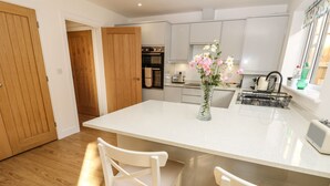A modern kitchen with a central island, white cabinetry, and a wooden door. - Larch Lodge (Totland Bay)