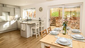 A modern kitchen with white cabinetry, a central island, and a dining area with a wooden table set for four. - Larch Lodge (Totland Bay)
