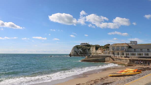 A coastal scene with a sandy beach, a rocky cliff, and a building with a balcony overlooking the sea. - Larch Lodge (Totland Bay)