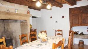 A dining room with a table set for four, wooden chairs, a patterned tablecloth, a chandelier, and a wooden cabinet. - House (Thenon)