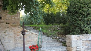A stone staircase leading up to a building with a metal railing and a green pot of red flowers at the bottom. - House (Thenon)