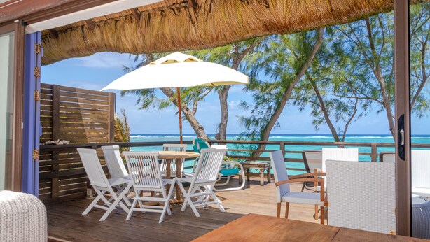 A wooden deck with white wicker furniture, a thatched roof, and a view of the ocean. - Spacious villa set in the turquoise lagoon of Trou d'eau Douce (Trou d'Eau Douce)