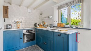A kitchen with blue cabinets, a white countertop, a built-in oven, a window with a view of greenery, and a hexagonal tile backsplash. - Luxury self-contained cottage for two with wood fired hot tub (Staverton)