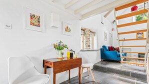 A modern living space with a wooden table, white chairs, a blue sofa, and a staircase. - Luxury self-contained cottage for two with wood fired hot tub (Staverton)