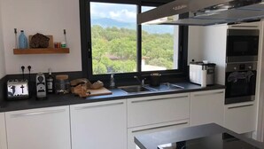 Een moderne keuken met witte kastjes, een zwart aanrecht, een ingebouwde oven en een raam met uitzicht op groen.