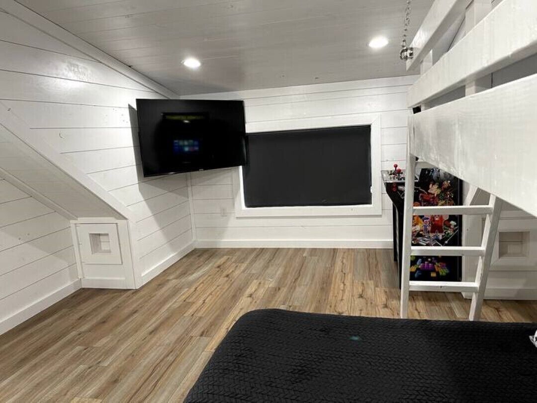 Una stanza con soffitto spiovente, TV a parete, una finestra e un letto a castello con ripiani contenitori.
