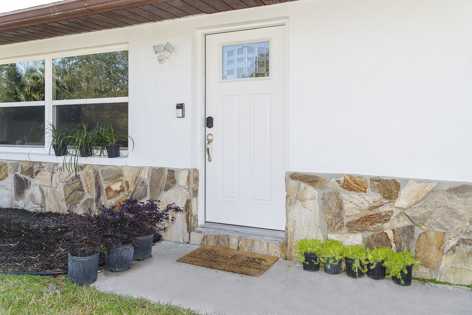 A house with a stone exterior, a white door, and potted plants around the entrance.