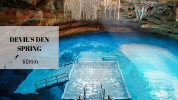Recorrido de 60 minutos por Devil's Den Spring, que muestra una escalera de madera que desciende hacia una piscina azul cristalina rodeada de paredes rocosas y estalactitas.