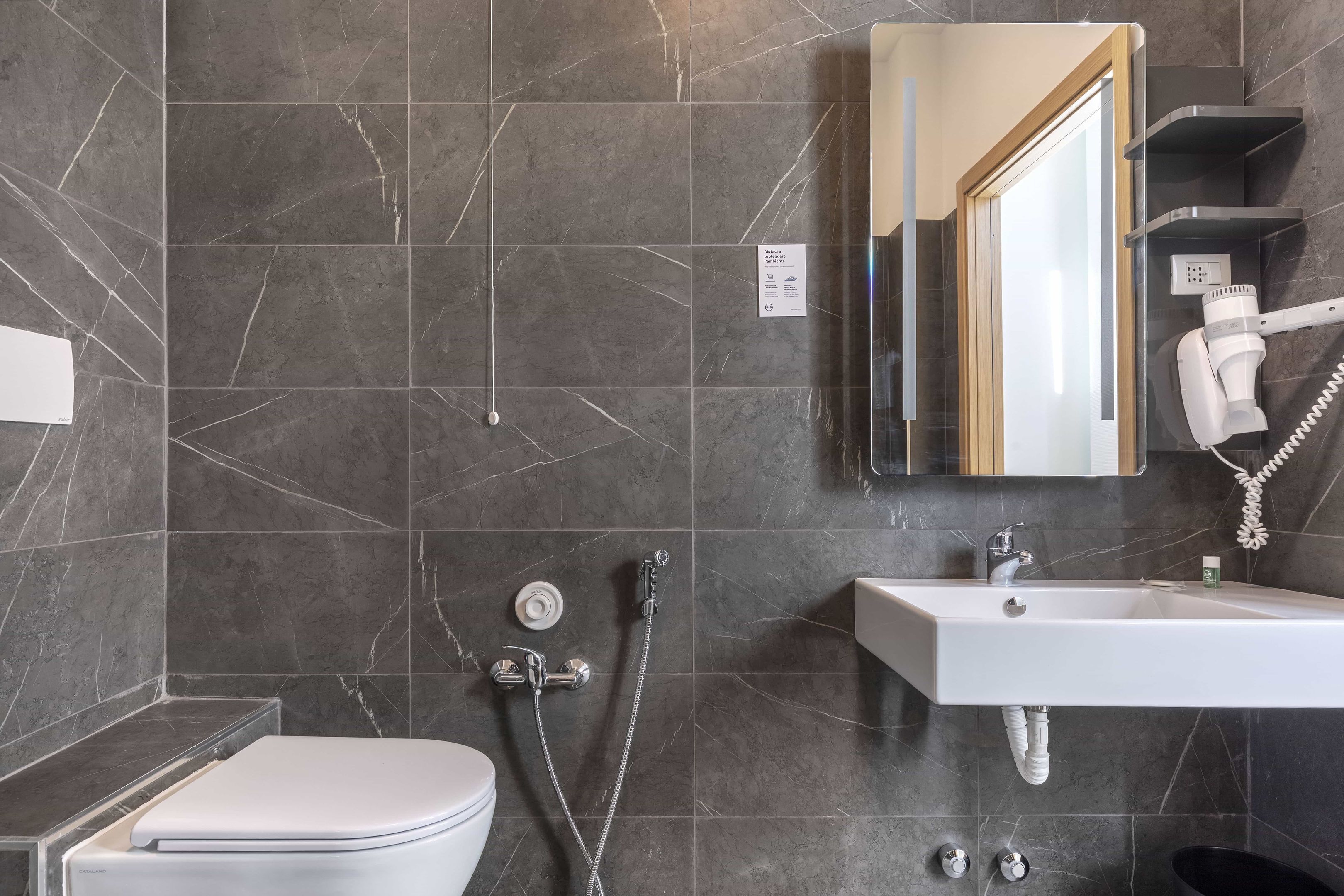 A modern bathroom with a toilet, a sink, a shower, and a mirror.