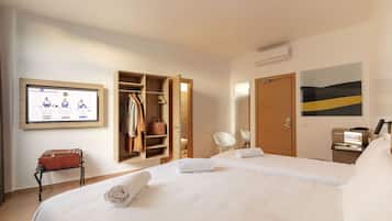 Una camera d'albergo con un letto grande, un armadio, una scrivania con un computer e una televisione a parete.