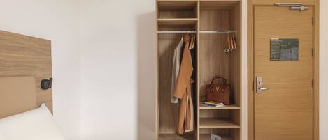 Una habitación de hotel con un armario de madera, una cama con ropa de cama blanca y un cabecero de madera.