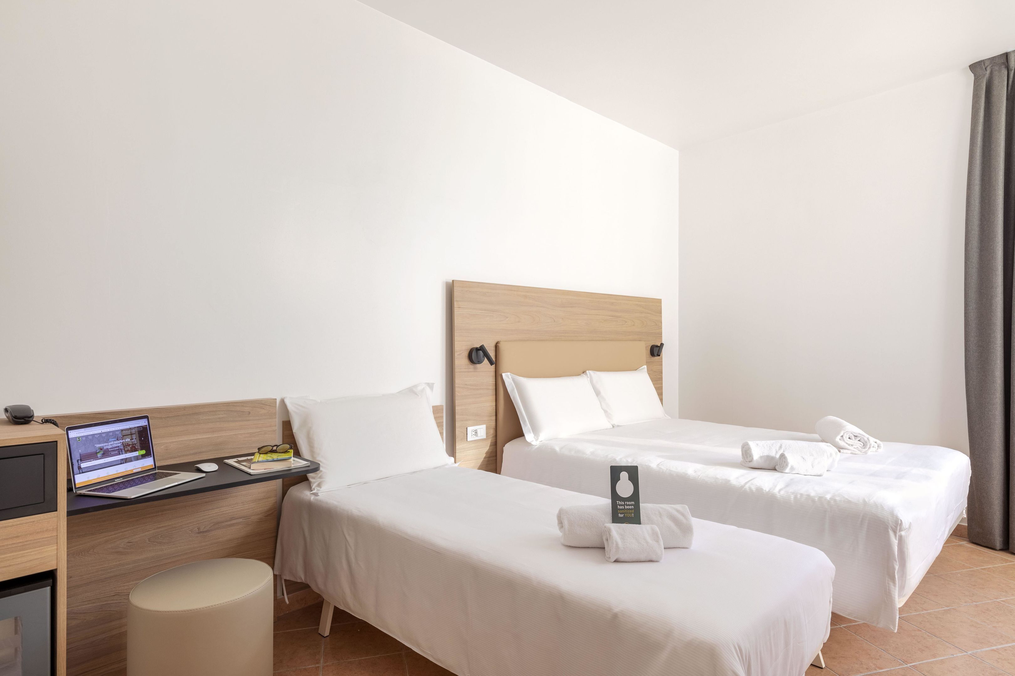 Une chambre d’hôtel avec deux lits simples, un bureau avec un ordinateur portable et un petit tabouret.