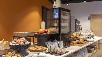 Ein Buffet mit verschiedenen Backwaren, darunter Gebäck, Muffins und eine Torte, präsentiert auf einer Theke mit einer Glastheke im Hintergrund.