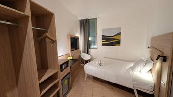 Habitación de hotel con cama, escritorio con computadora, armario y ventana con cortinas.