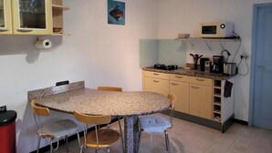 Cocina compacta con encimera de granito, cocina a gas, microondas y pileta. Hay dos sillas de madera y una mesita.